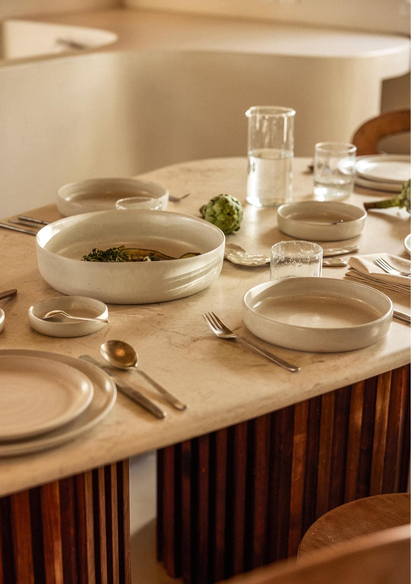 A set table with beige ceramics. Also water carafes and artichokes.