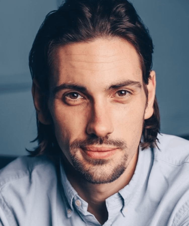 Portrait of a middle-aged man with long black hair, he looks directly at the camera and smiles.