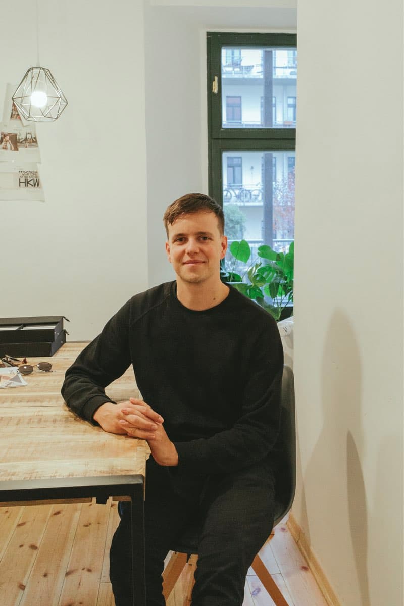 Portrait eines jungen Mannes mit braunen Haaren. Er sitzt an einem Tisch, gemütliche Atmosphäre.